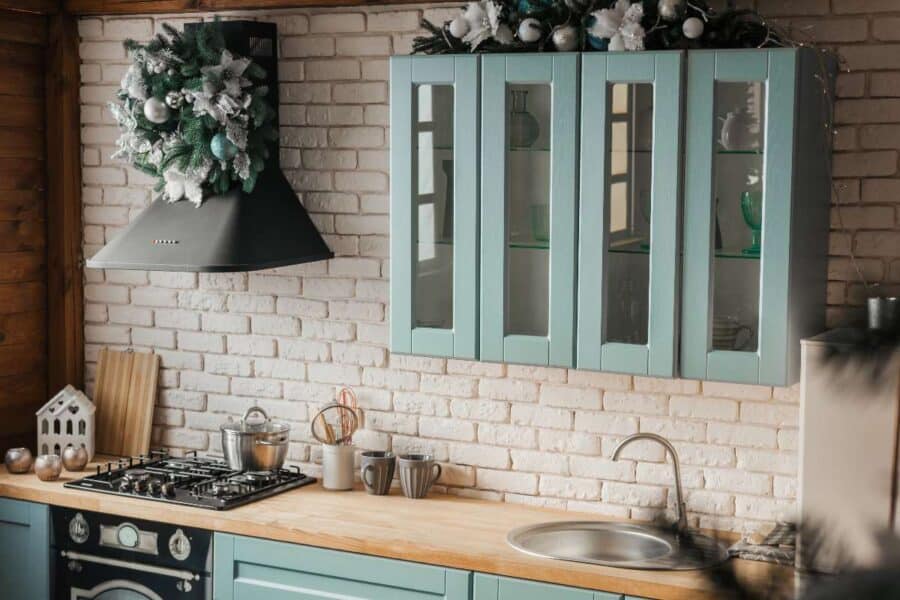 Festive kitchen with pastel blue cabinets, white brick walls, and wood countertops decorated for Christmas.