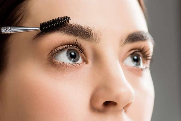 Woman brushing her brows with a spoolie – shaping eyebrows for a balanced, natural look.
