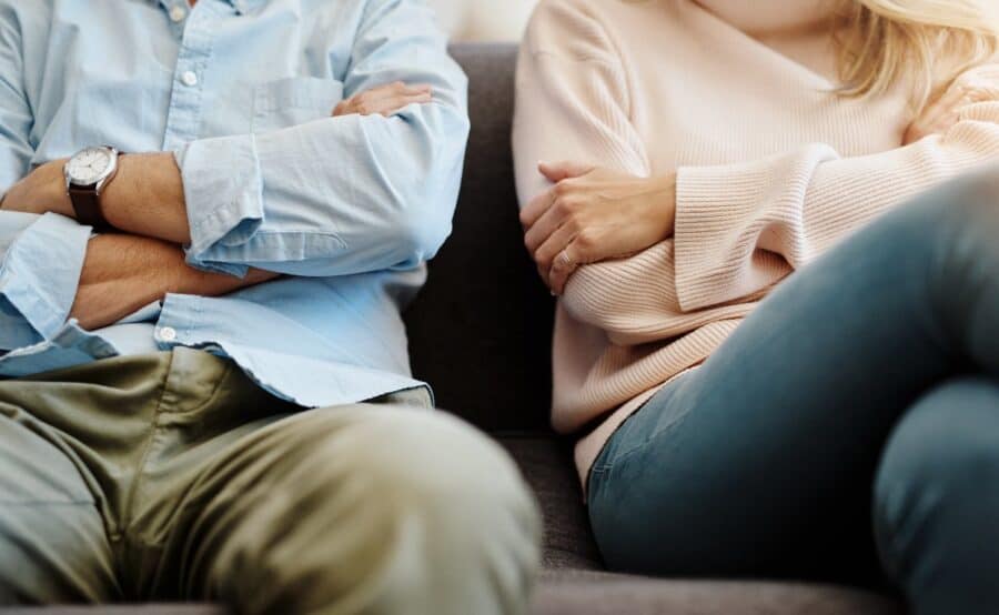 Couple sitting apart on sofa with arms crossed, symbolising emotional distance while exploring legal options for divorce in Australia.