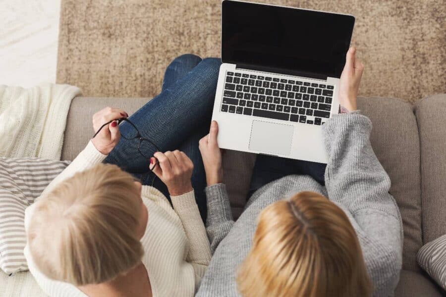 Two women sitting on a sofa looking at a laptop screen together.