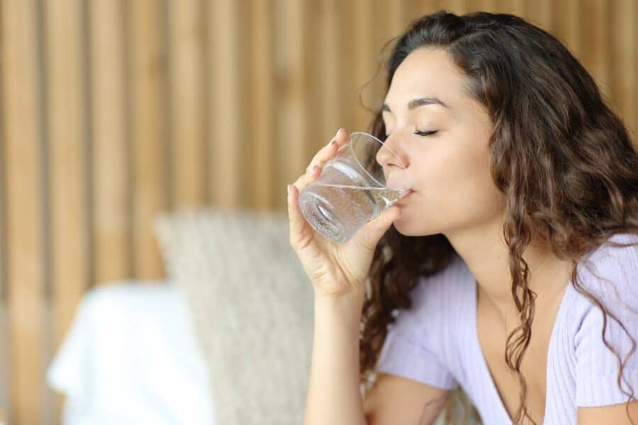 Woman drinking a glass of water in the morning to boost energy naturally.