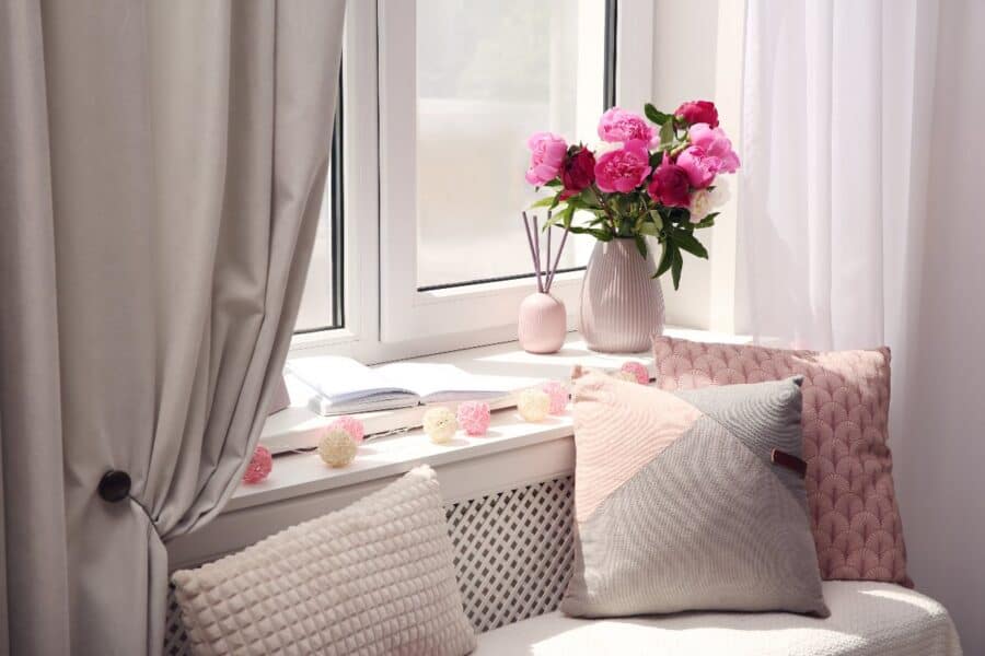 Cosy window seat book nook with pink cushions, fresh flowers, and an open book