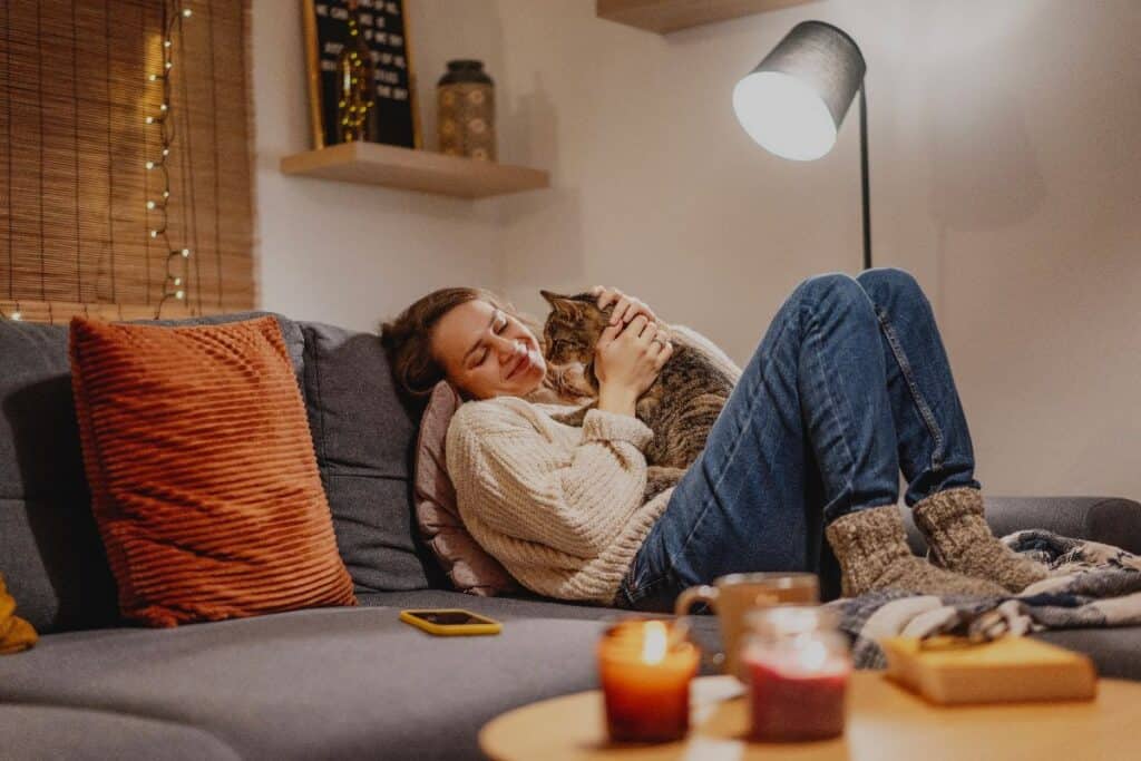 Cosy sofa scene with warm lamplight, candles and a cat cuddle—simple sleep cues for autumn evenings before bed.