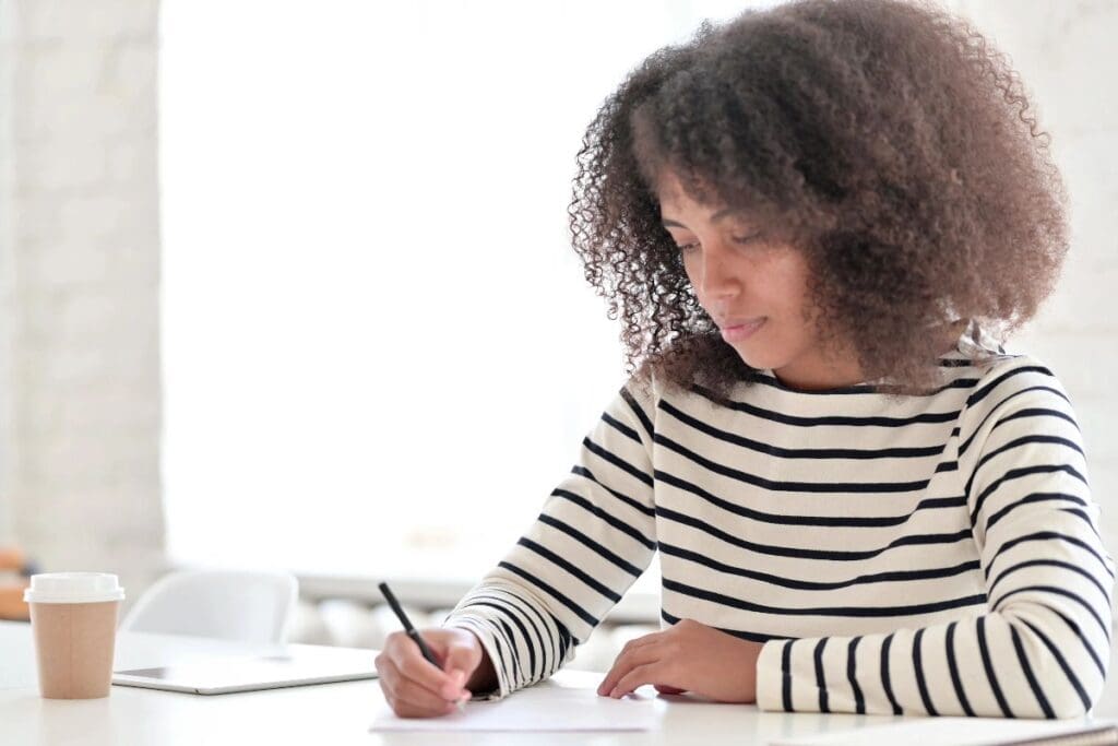 Woman doing a brain dump for anxiety, writing thoughts on paper at a bright white desk.