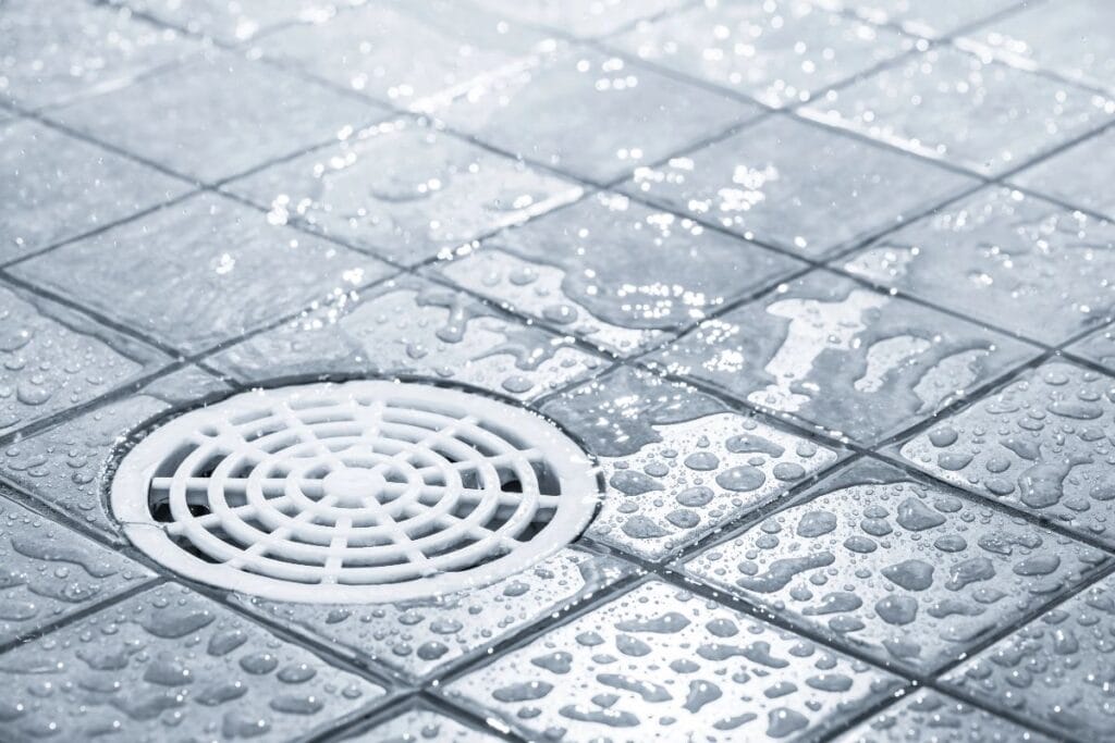 Close-up of a wet tiled shower floor with a round drain, showing why choosing a shower drain that clears water quickly matters.