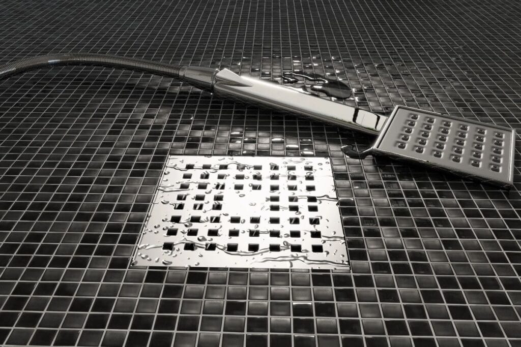 Modern walk-in shower floor with black tiles, chrome handheld shower and square drain, showing the importance of choosing a shower drain that drains fast.