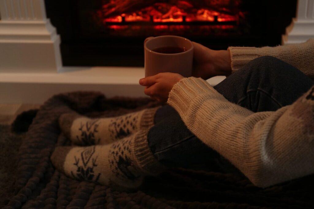 Person in cosy winter socks sitting by the fire with a hot drink, creating a calm winter mindset before bedtime.