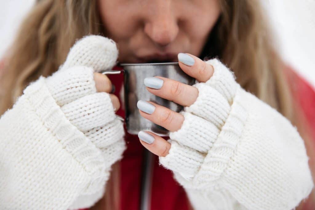 Close-up of a woman in winter gloves holding a hot drink outdoors, taking a quiet moment to protect her winter mindset and warm up.