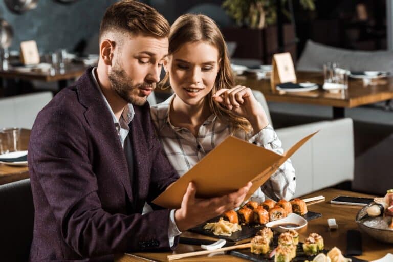 Couple choosing from a menu at a modern sushi restaurant, illustrating UK Restaurant Gift Vouchers as a flexible gift idea
