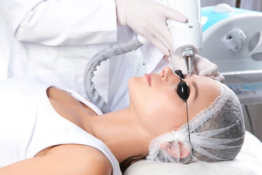 Clinician performing laser microblading removal on a client’s eyebrows while the client wears protective eye shields.