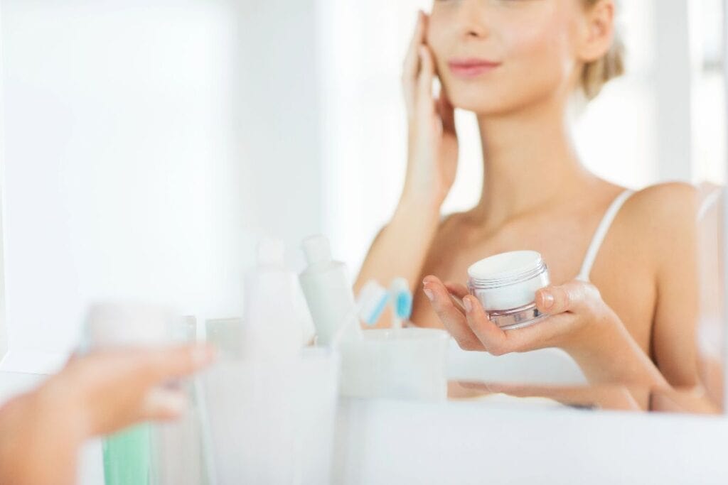 Woman applying face cream in front of a bathroom mirror, refreshing your skincare routine with a new moisturiser.