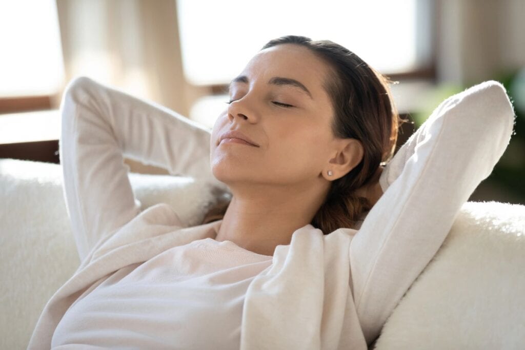 Woman relaxing on a sofa with eyes closed, taking a calm mindful break
