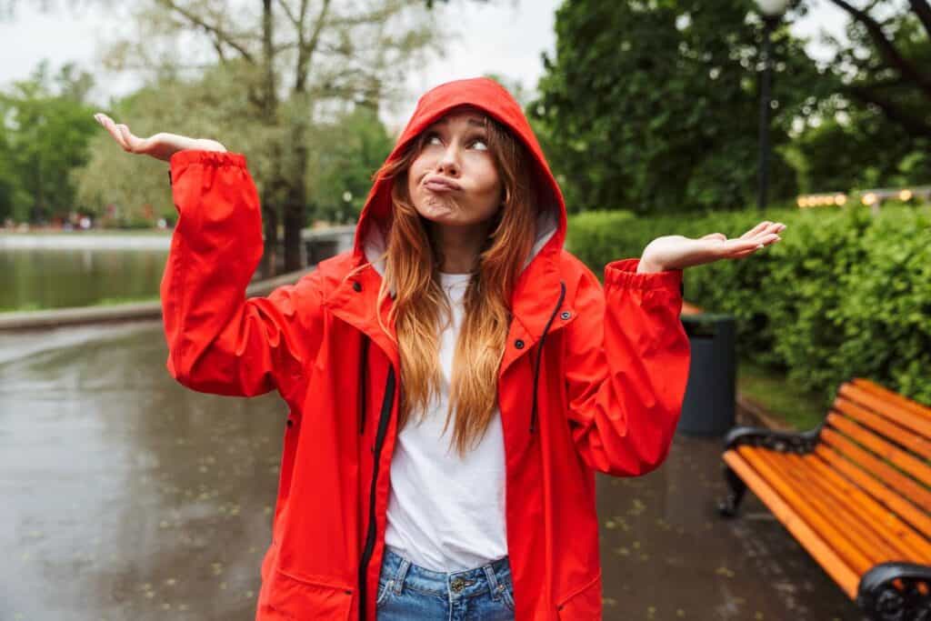 Woman in red rain jacket shrugging in wet park – how to dress for British weather