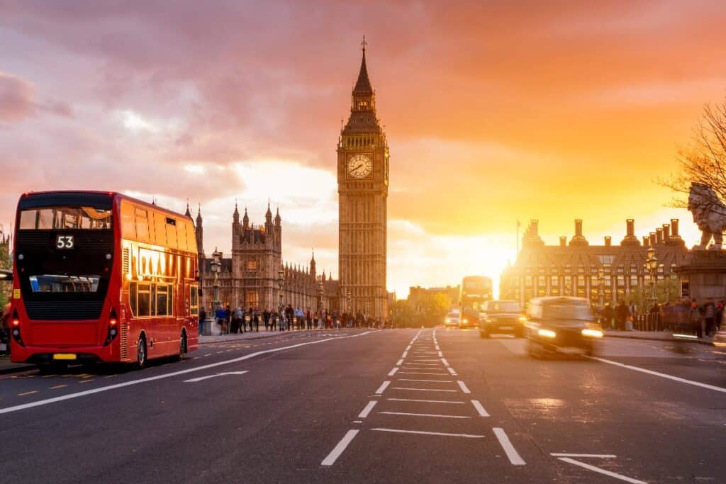 Red London bus driving past Big Ben in Westminster at sunset