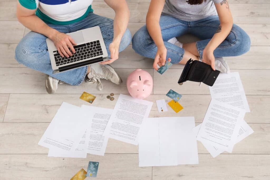 People creating a household budget on the floor with bills, bank cards, a laptop and a piggy bank