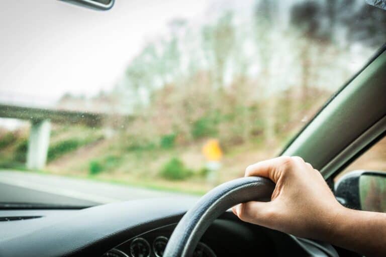 Driver’s hand on steering wheel on a road, driving in the UK for the first time guide