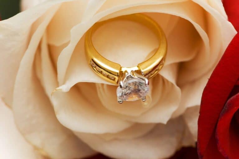 Gold solitaire diamond engagement ring resting on a white rose.