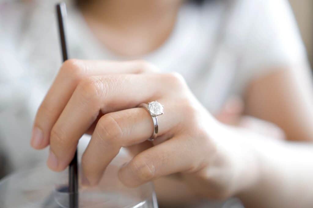 Hand wearing a solitaire diamond engagement ring while writing, showing everyday wear.