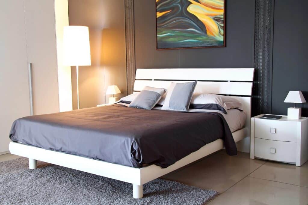 Modern bedroom with white bed frame, matching bedside tables and floor lamp in a spacious layout