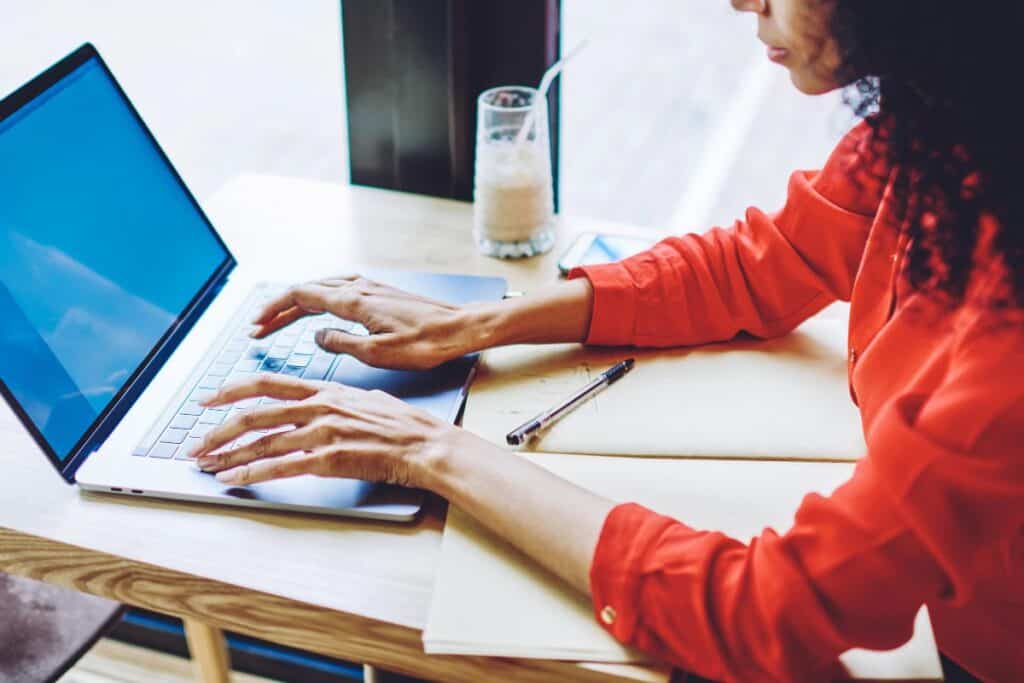 Remote worker typing on a laptop with notes on a desk