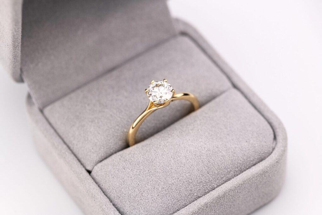 Gold solitaire diamond engagement ring in a grey velvet ring box.