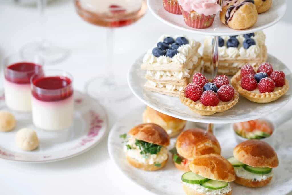Tiered cake stand with cucumber sandwiches, fruit tarts and mini desserts — a classic British afternoon tea spread.