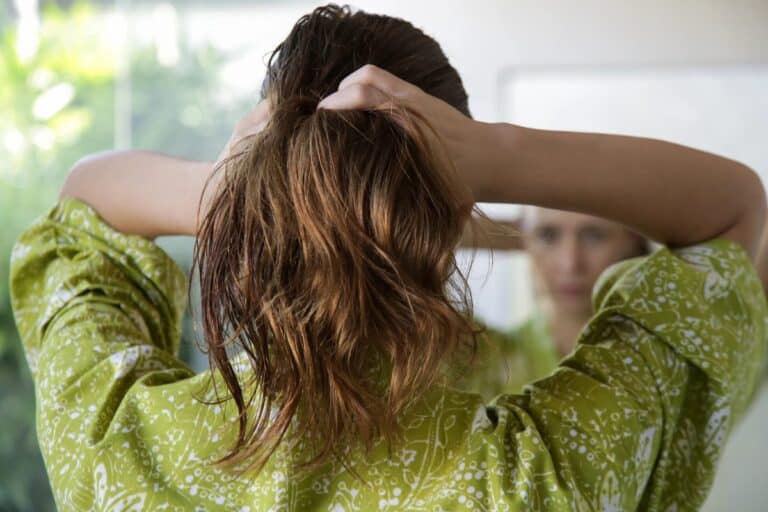 Woman gathering her long hair into a quick updo during a busy morning routine.