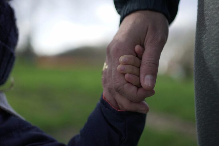 Parent gently holding a child's hand outdoors, illustrating how to support a grieving child with steady presence and love.