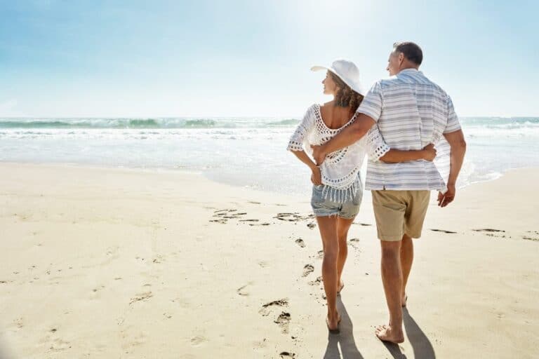Couple walking along a sunny beach to show why holidays are important for rest and wellbeing.