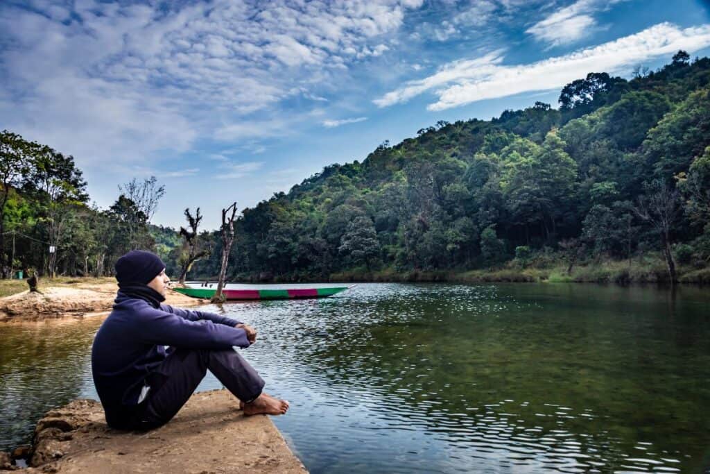 Person sitting quietly by a lake in nature, showing the calming mental health benefits of taking a holiday.