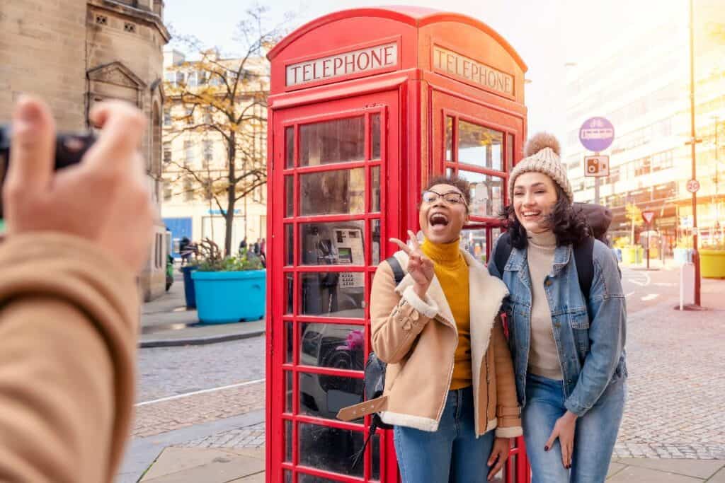 Two friends laughing and posing for a photo in front of an iconic red British telephone box in London — capturing the fun of using British slang.