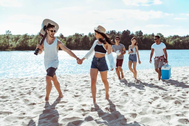 Group of friends in cute beach day outfits walking along sandy beach on a sunny summer day