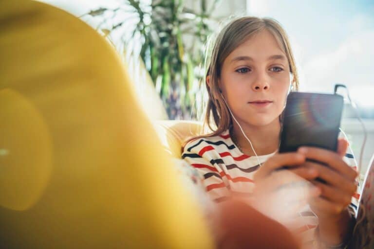 Young girl using a smartphone with headphones at home — online safety tips for UK parents.