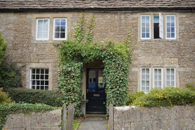 Old UK stone cottage with original timber sash windows and climbing greenery around the front door.