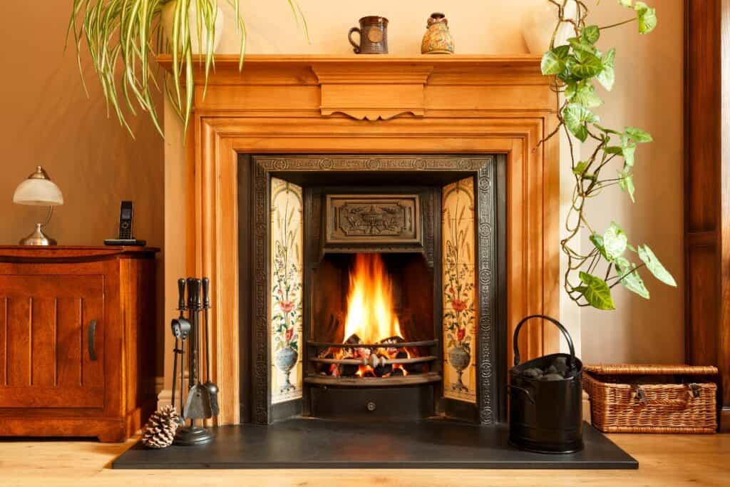 Lit Victorian fireplace with cast iron insert and tiled surround in a warm UK period home.
