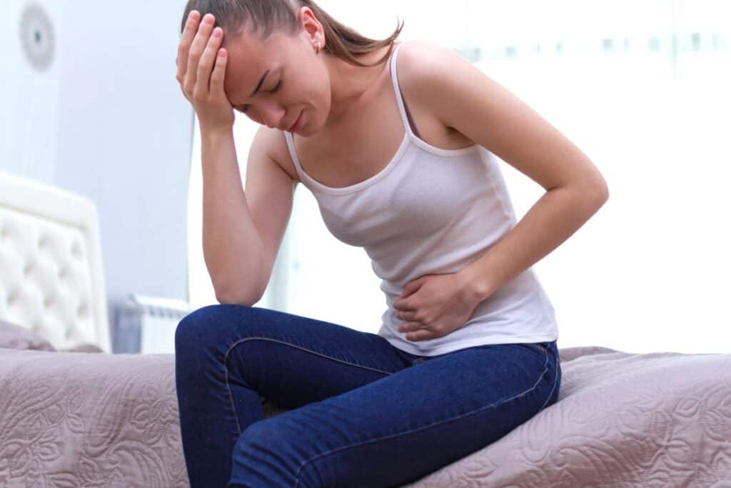 Woman sitting on a bed holding her stomach with possible UTI discomfort.
