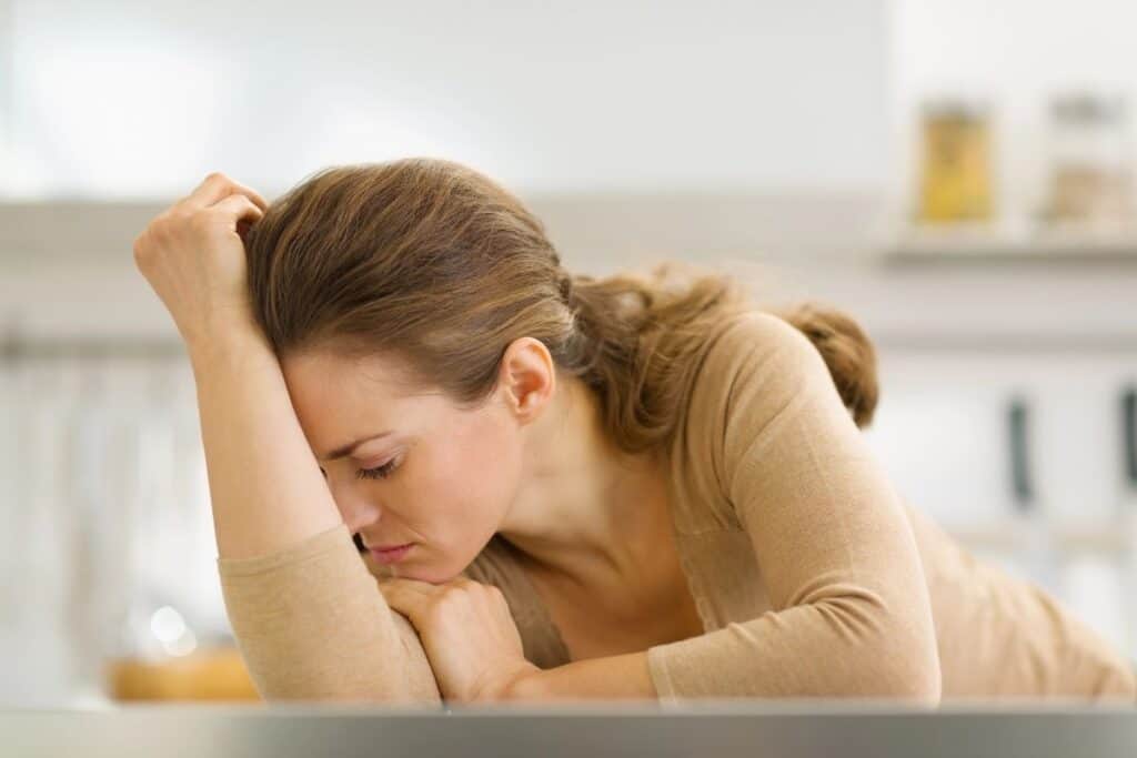 Woman leaning on a kitchen counter looking thoughtful and overwhelmed.