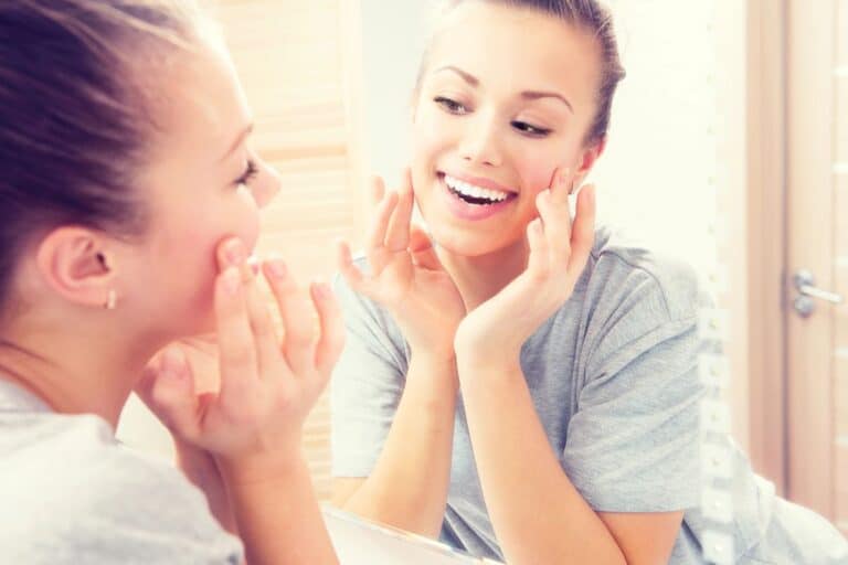 Young woman applying skincare in a mirror for a guide to K-beauty ingredients for sensitive teen skin.