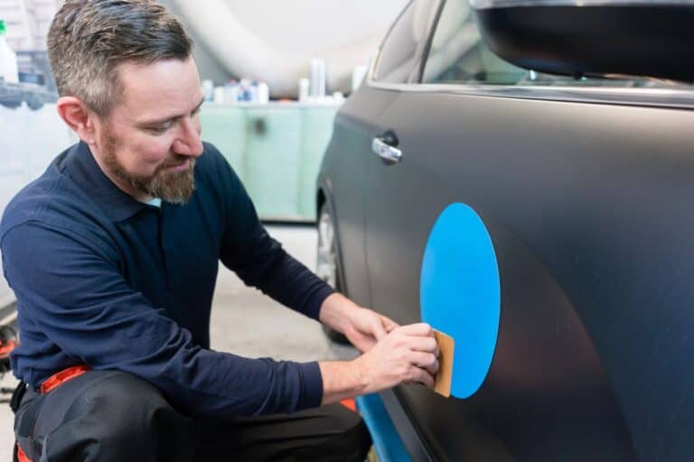Man applying a blue decal to a car door to personalise the vehicle.