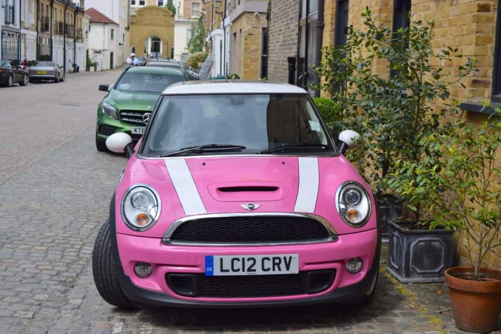 Pink car parked on a UK street with a front number plate visible.