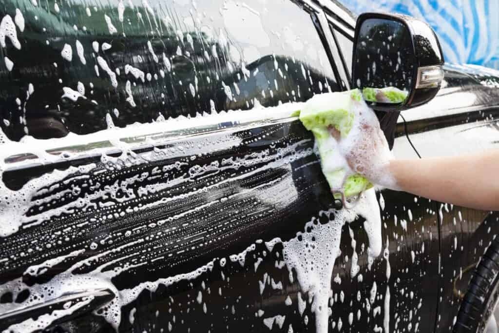 Person washing a black car with soap and a sponge.