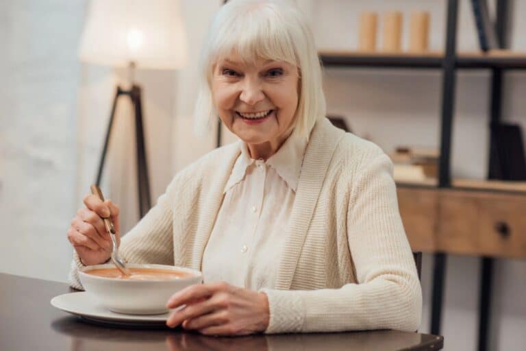 Older woman sitting comfortably at home eating a meal independently.