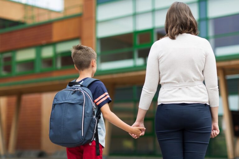 Parent holding a child’s hand outside school during the back-to-school rush