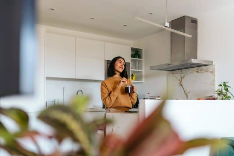 Woman holding a drink in a bright kitchen as part of a simple wellbeing routine.