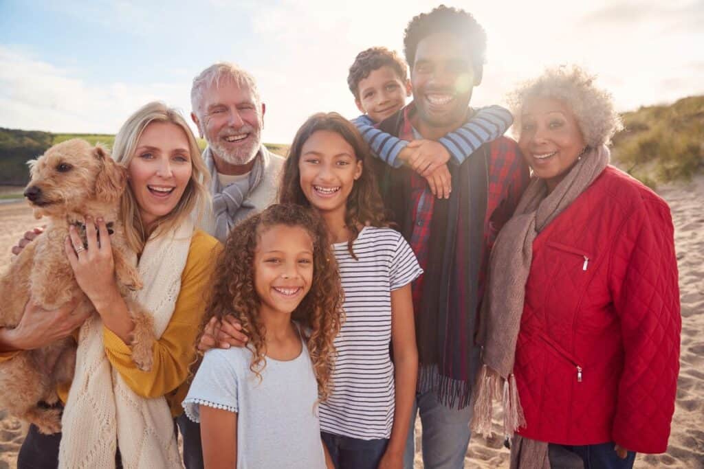 Multi-generational family smiling together on a beach holiday with a dog.
