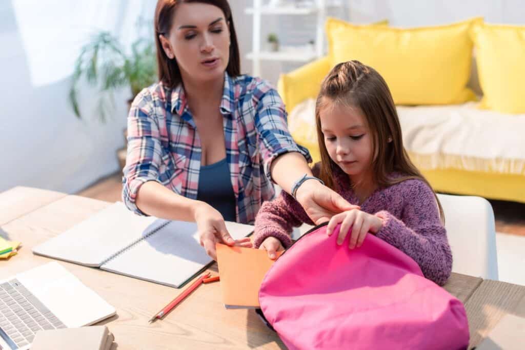 Parent helping her daughter pack a school bag before returning to school