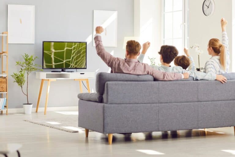 Family sitting on a sofa watching football on TV at home.