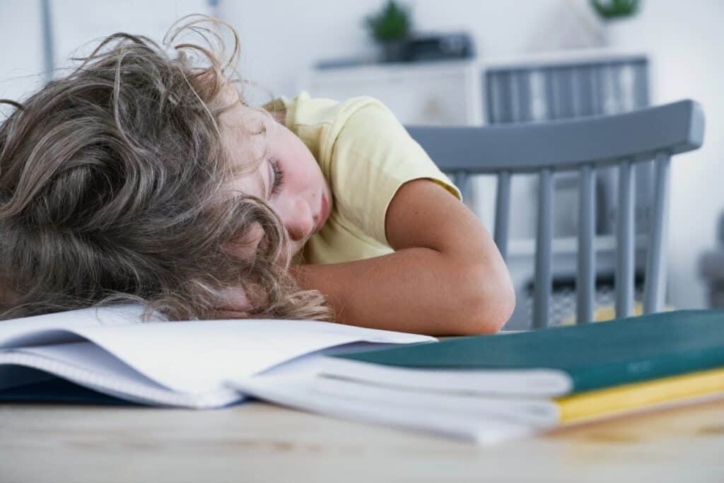 Tired child asleep at a table beside school books after returning to school