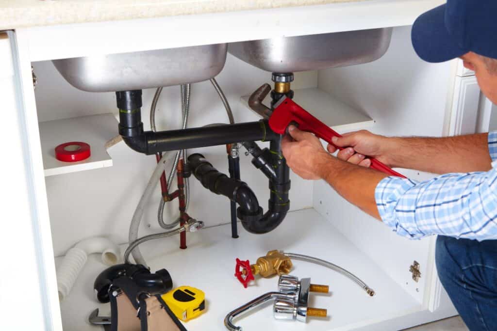 Plumber working on pipes under a kitchen sink to fix a blocked drain.