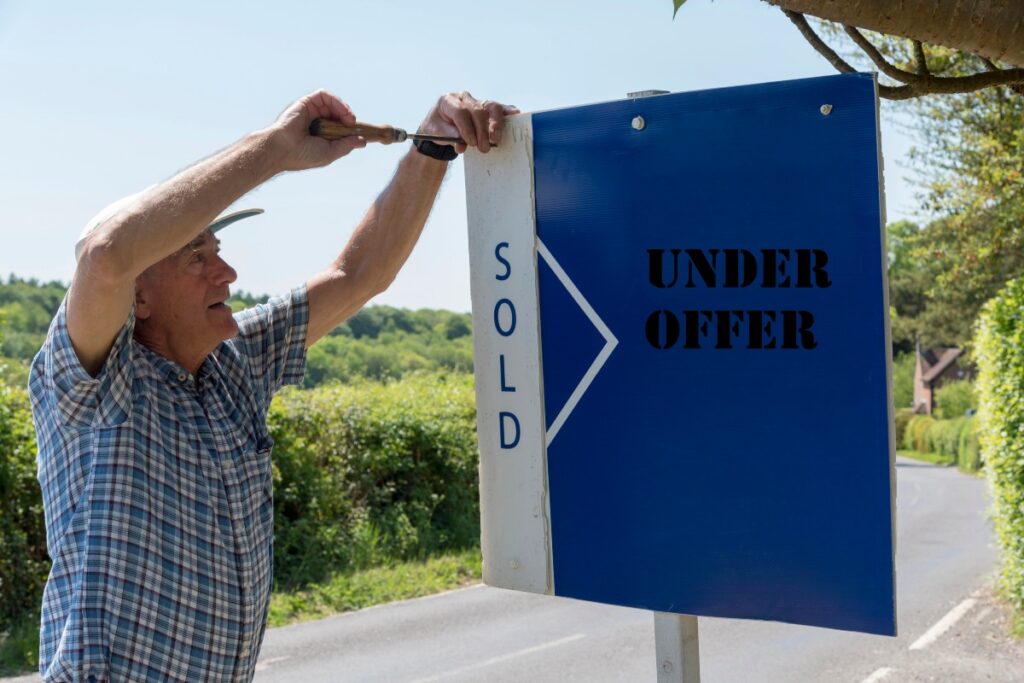 Man putting an under offer sign on a house for sale in spring.